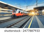 High-speed orange passenger train moving at railway station platform at sunset. Train station. Modern railway transportation concept with blurred motion effect. Railroad. Commercial transport