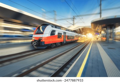 High-speed orange passenger train moving at railway station platform at sunset. Train station. Modern railway transportation concept with blurred motion effect. Railroad. Commercial transport