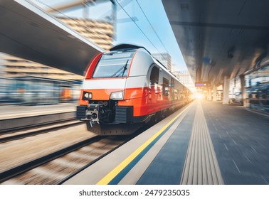High-speed orange passenger train moving at railway station platform at sunset. Train station. Modern railway transportation concept with blurred motion effect. Railroad. Commercial transport