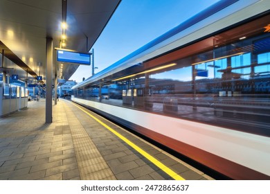 High-speed passenger train in motion at the illuminated railway station at night. Moving white modern intercity train, railway platform, architecture, lights. Train station in Graz, Austria. Railroad	 - Powered by Shutterstock