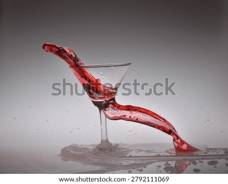 High-speed studio photography of a glass with dramatic water  splash and colored liquid splash, frozen in motion against a clean gray background. Abstract beverage concept with dynamic droplets, reflection, and elegant fluid movement.