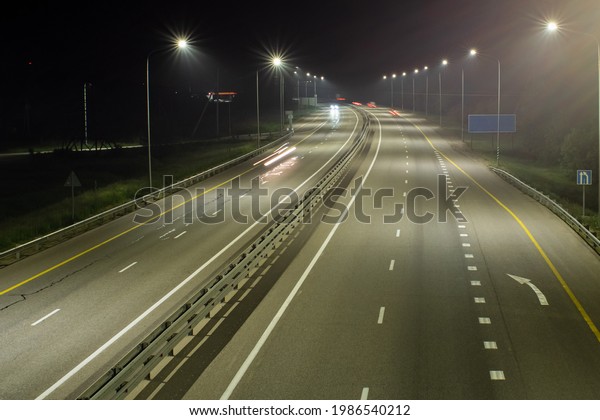 High-speed suburban highway in the light of\
streetlights. There are yellow and white markings on the asphalt.\
There are signs on the side of the\
road
