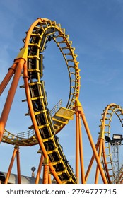 High-speed Thrilling roller coaster loop at an amusement park with bright colors and curved tracks against a clear blue sky.