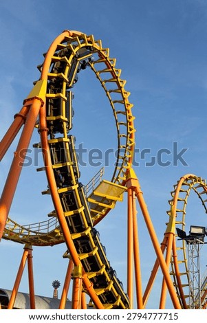 High-speed Thrilling roller coaster loop at an amusement park with bright colors and curved tracks against a clear blue sky.