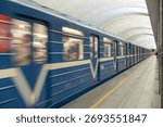 A high-speed train moves through an underground metro station. A modern passenger car with motion blur effects on a railway platform
