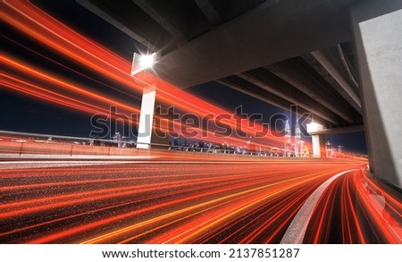 High-speed vehicles bright light trails on asphalt road under the flyover at night.