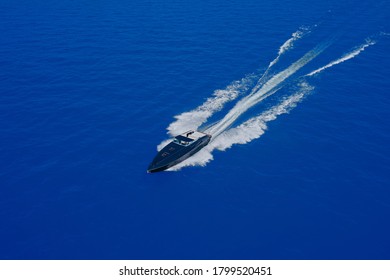 High-speed Yacht Of Blue Color Fast Motion On Blue Water In The Rays Of The Sun Top View. Speed Boat Movement At High Speed Aerial View.