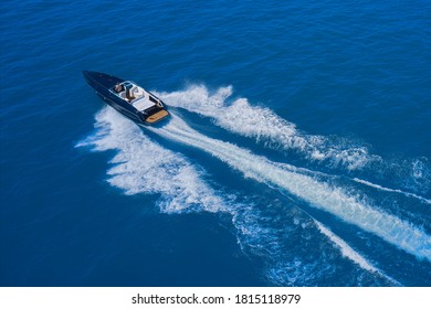 High-speed yacht of blue color fast motion on blue water in the rays of the sun top view.  Speed boat movement at high speed aerial view. Top back view of the boat.