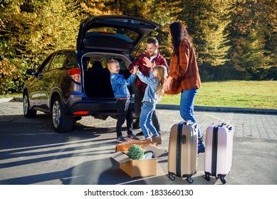 High-spirited likable parents unloading the auto's trunk with their cute 10-12s kids during moving into new apartment. - Powered by Shutterstock