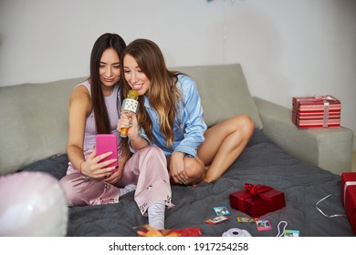 High-spirited Woman With A Karaoke Wireless Microphone Staring At The Cellphone Screen In Her Friend Hands