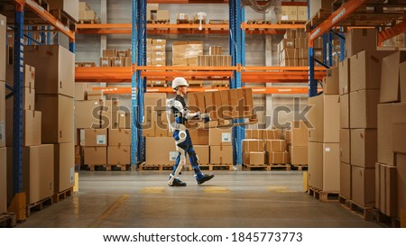 High-Tech Futuristic Warehouse: Manager Scans Packages for Inventory, Delivery in the Background Worker Wearing Advanced Full Body Powered exoskeleton, Walks with Heavy Pallet full of Cardboard Boxes