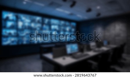 A high-tech security operations center features a massive video wall displaying multiple surveillance feeds and a central desk with computers.