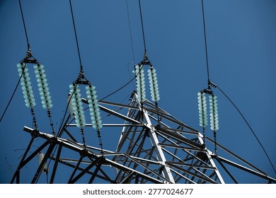 High-voltage power line tower with insulators against blue sky background, renewable energy, infrastructure, electrical transmission, utility, modernization, technology, power grid, engineering, rural setting
