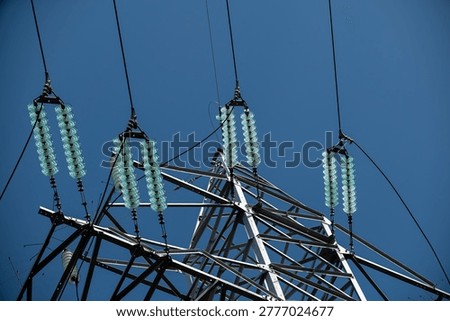 High-voltage power line tower with insulators against blue sky background, renewable energy, infrastructure, electrical transmission, utility, modernization, technology, power grid, engineering, rural setting
