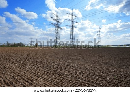 A lot of high-voltage power line, transmission tower overhead line masts, high voltage pylons as power pylons on the fields