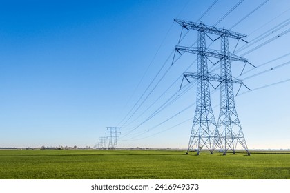 High-voltage pylons and lines contrasting against a blue sky. The masts are positioned on a vast agricultural grassland. The photo was taken in the Netherlands on a sunny day in the winter season. - Powered by Shutterstock