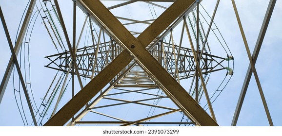The high-voltage tower is inside. Metal structures going up against the background of blue sky with clouds. Electrical insulators and wires. Sunny day.