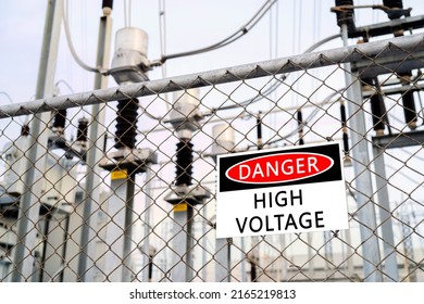 Subestación de transformador de alta tensión detrás de la valla de enlace de cadena de alambre de púas con señal de alto voltaje de peligro.