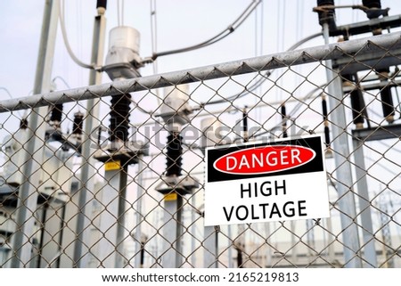 High-voltage transformer substation behind barbed-wire chain-link fence with Danger High Voltage sign.
