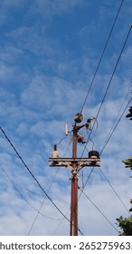A high-voltage utility pole featuring multiple ceramic insulators, transformers, and electrical components, set against a vibrant blue sky with scattered clouds. This image captures the essential infr