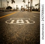 Highway 101 sign painted on the black asphalt road with city diffused in the background. The shot is from Oceanside California