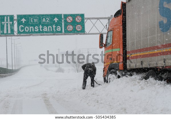 Highway A2, Romania, 17 January 2016: A truck\
driver shovels snow to free his truck on the closed highway A2, the\
main commercial route which connects Bucharest to the Black Sea\'s\
port, Constanta.