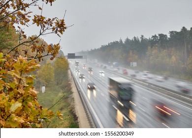 The highway A3 near Nuremberg with many cars with lights switched on driving with speed on a rainy day in wet conditions in  November with autumn forest around
