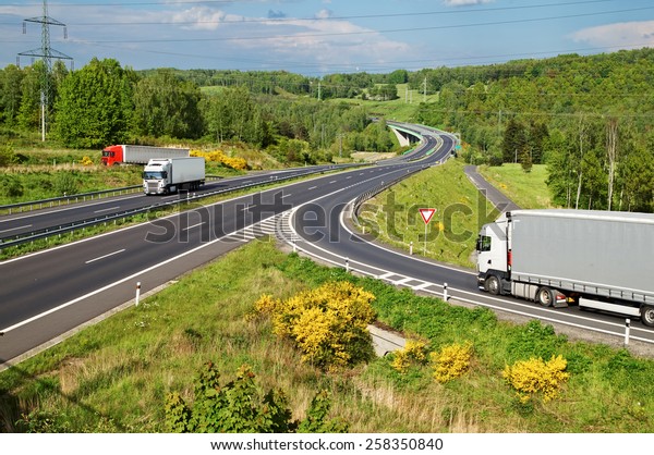 Highway in the\
countryside. Three moving trucks. Electronic toll gate and a bridge\
in the distance. View from\
above.