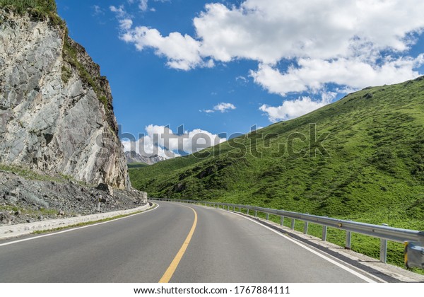 Highway curves in the background of\
mountains and grasslands in Xinjiang, China in\
summer