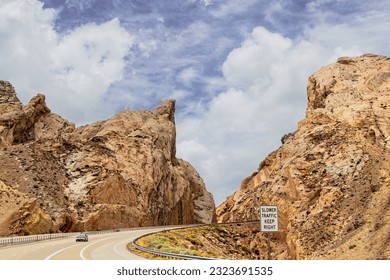 Highway cut through weirdly shaped  barren mountains with car making curve and sign saying Slower Traffic Keep  Right. USA