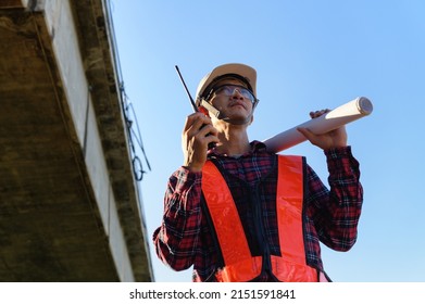 Highway Engineer Standing To Use Walkie Talkie And Drawing Paper Roll Under Old Concrete Bridge