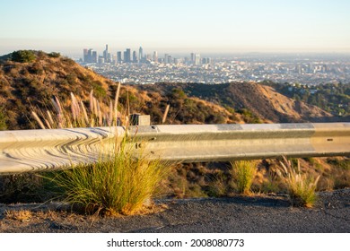 Highway guardrail barrier on road leading to the top of Mount Lee in Santa Monica mountains. Blurred Los Angeles downtown skyscrapers on horizon.