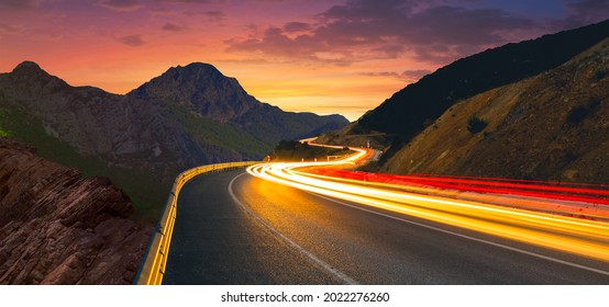 Highway landscape at dusk. Traffic view from world highways. Fantastic image of cars speeding through the highway between mountains at sunset. car lights on the road.. - Shutterstock ID 2022276260
