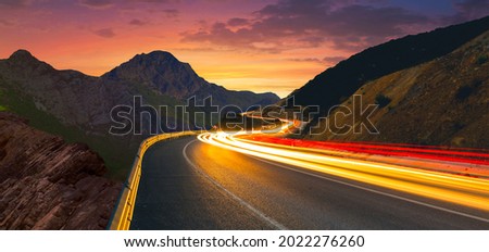 Highway landscape at dusk. Traffic view from world highways. Fantastic image of cars speeding through the highway between mountains at sunset. car lights on the road..