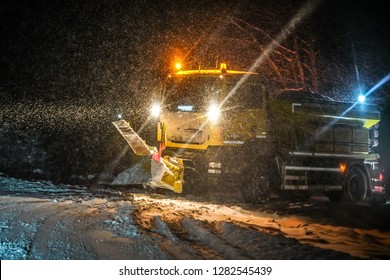 Highway maintenance truck cleaning road during heavy snowstorm in night, dangerous driving during winter transport calamity.