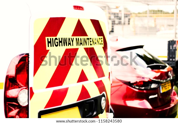 Highway Maintenance Vehicle parked on the road next\
to a red car