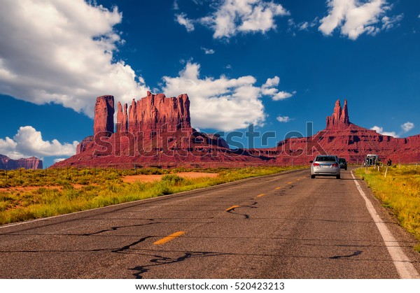 Highway in Monument\
Valley, Utah / Arizona, USA - Picture with road and cars driving\
towards the hills. Photo made during a road trip throughout the\
western states.