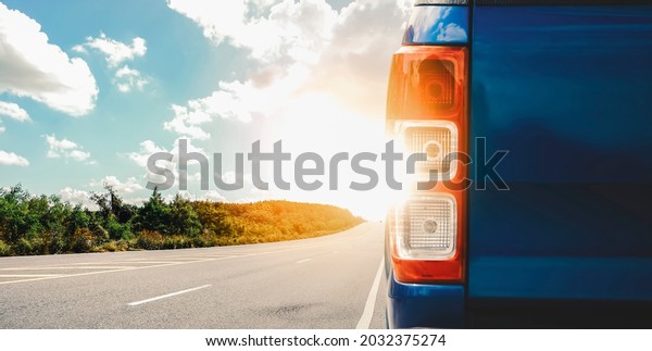 Highway with sunset and rear bumper of the blue\
car parked on the\
roadside