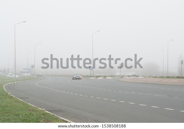 The highway traffic in heavy fog. Cars moving\
on the highway in poor\
visibility