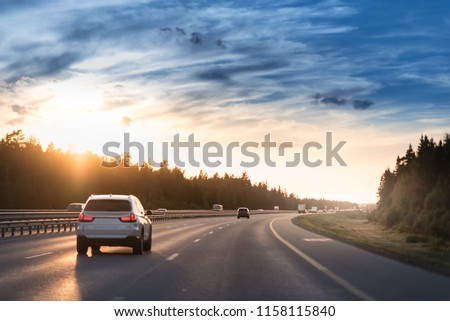 Highway traffic in sunset. Road with metal safety barrier or rail. cars on the asphalt under the cloudy sky.