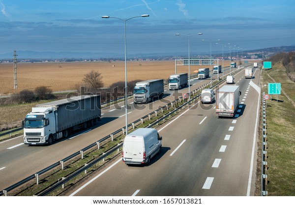 Highway\
transportation with a convoy of white Lorry trucks passing trucks\
and vans with a beautiful sunset\
sky