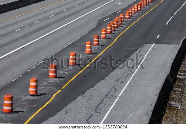Highway under construction with a concrete\
roadway repaved with black asphalt, and line of orange barrel\
cones, in a transportation\
background