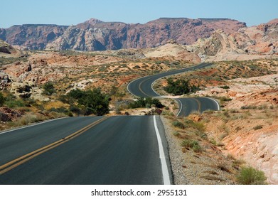 Highway Unfurls Like A Ribbon Across The Multi-Hued Desert Terrain