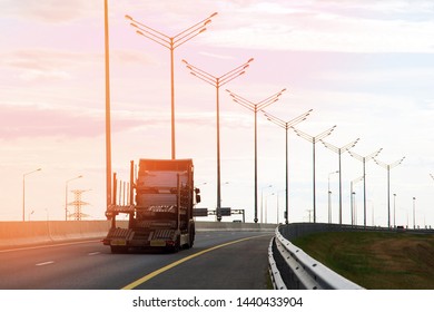 Highway View Against Evening Sky, Row Of Lampposts, Empty Car Transporter Truck Driving Away In Sun Glare