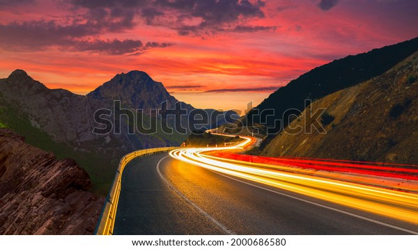 highway view at\
sunset. car lights form long colored lines on the highway. road\
view through mountains and colorful sunset view. European highways\
and mountains. Bavaria,\
Germany.
