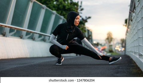 Hijab girl exercising on walkway bridge in early morning. Muslim woman wearing sports clothes doing stretching workout outdoors.