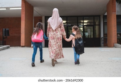 Hijab muslim mother walking her two children to school. Female muslim parent goes with kids girls to school.
