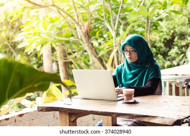 A hijab muslim woman using laptop on wooden table in the outdoor cafe - Powered by Shutterstock