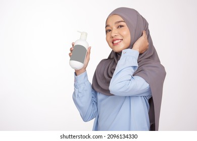 Hijab Woman Touching Her Head And Hold Bottle Shampoo And Conditioner. Happy Muslim Hijab Young Woman With Balm Bottle Applying Hair Mask. Hemp, Cbd Cosmetic Product.