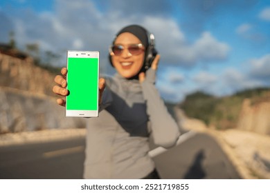 hijab woman wearing sportswear holding green screen phone for mockup - Powered by Shutterstock